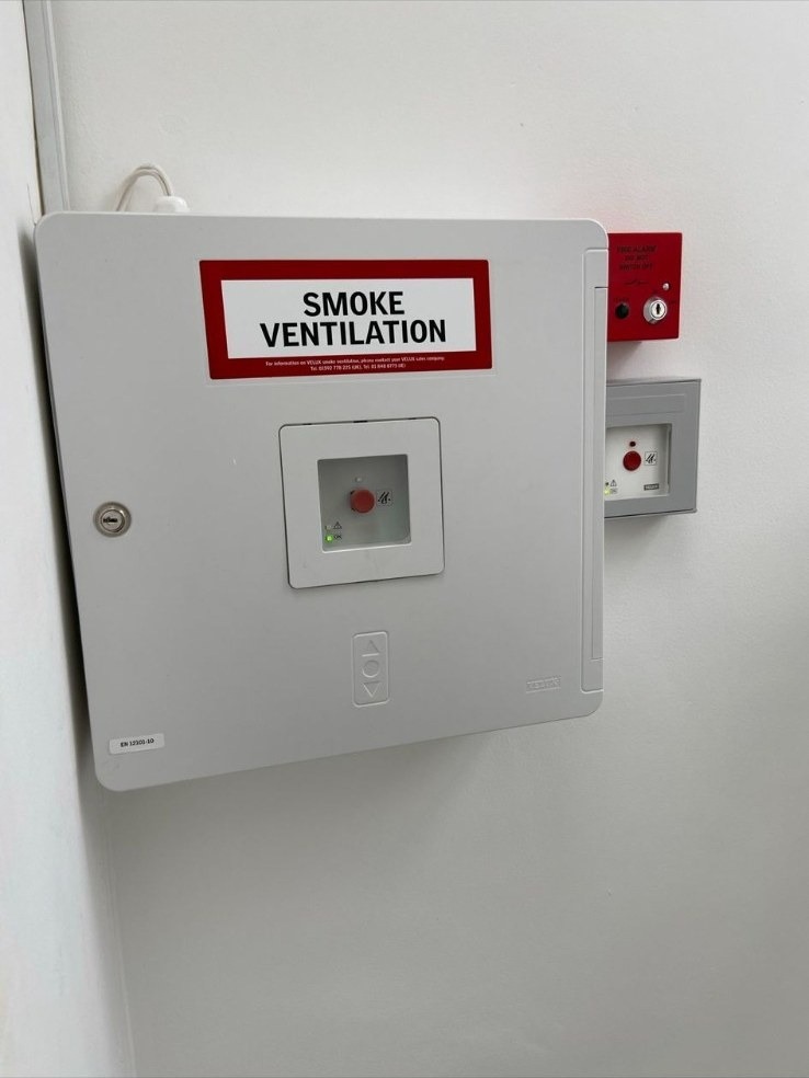 Smoke ventilation (AOV) control panel installed alongside a fire alarm manual call point on a commercial wall.